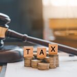 Tax law concept. Wooden blocks word " TAX" on coin stack .with gavel and money on the table.